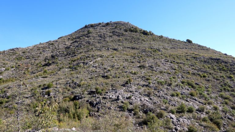 Blick von der vorgelagerten Anhöhe auf den Gipfel. Dazwischen eine Passage mit dornigen Sträuchern.